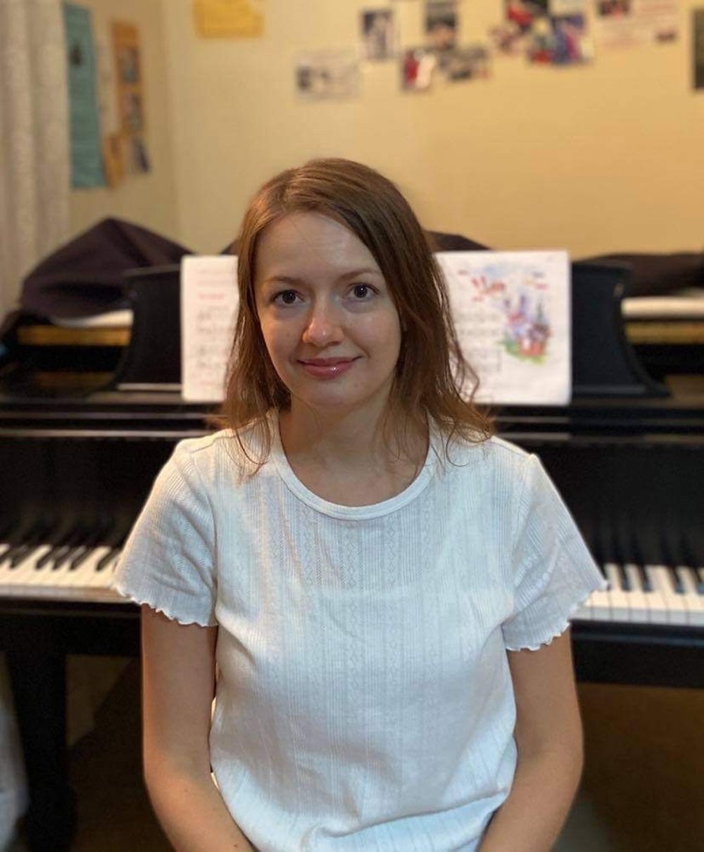 Anastasiya Nyzkodub seated in front of a grand piano with sheet music on the stand