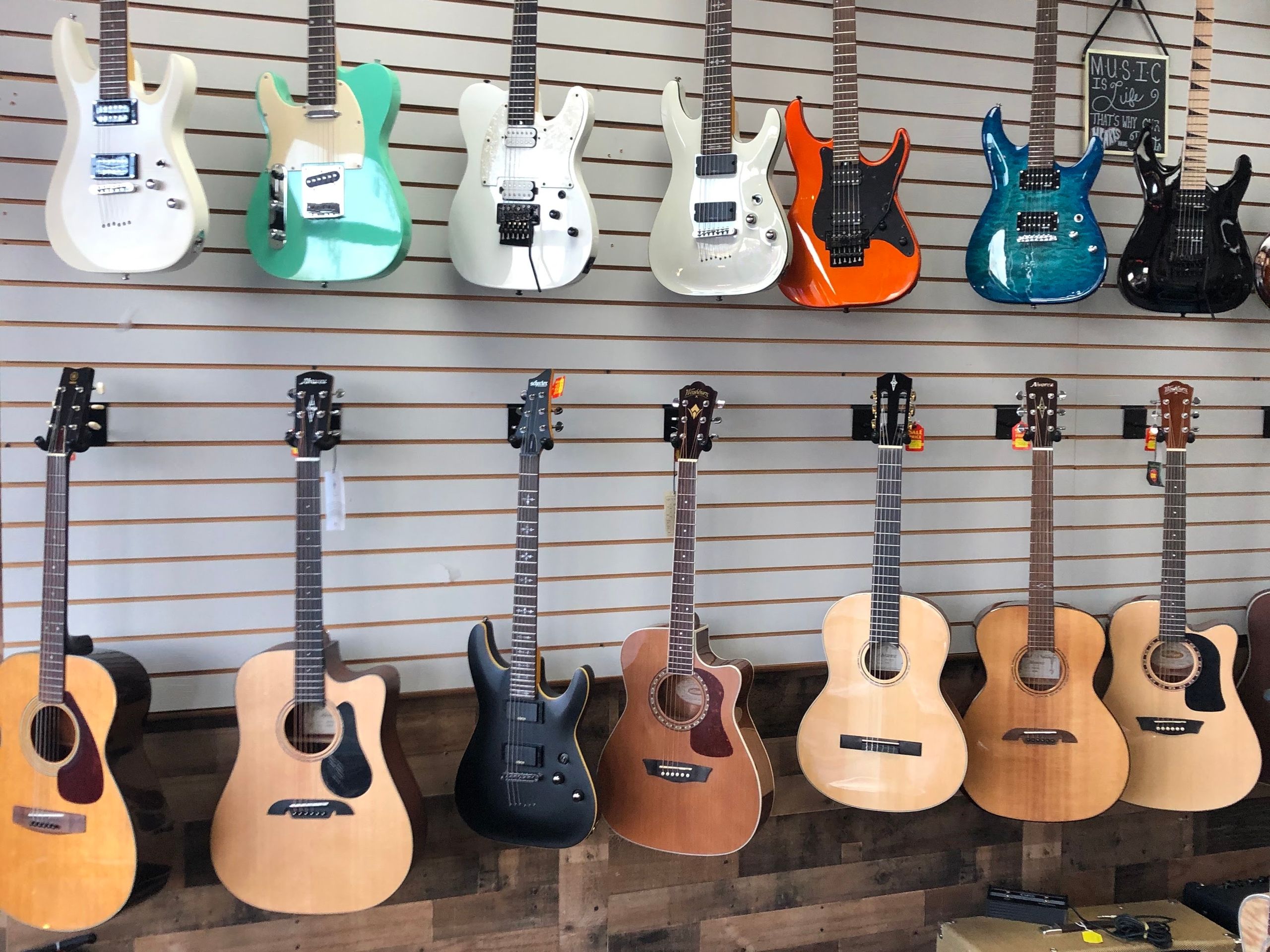 Electric and acoustic guitars filling the slatwall above the reclaimed wood base