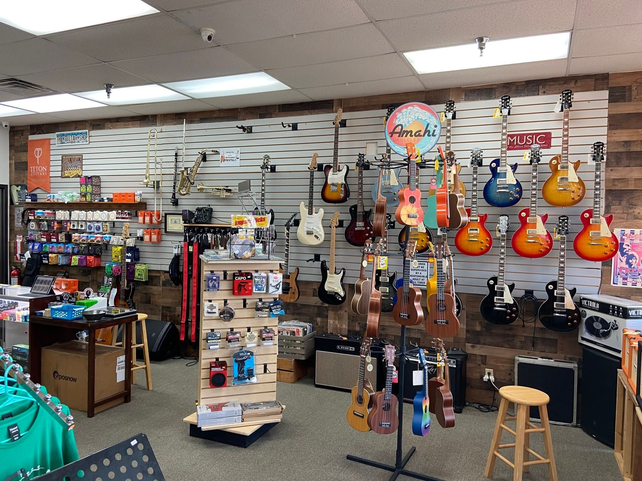 Electric guitars and ukuleles beside the accessory display and amp shelf