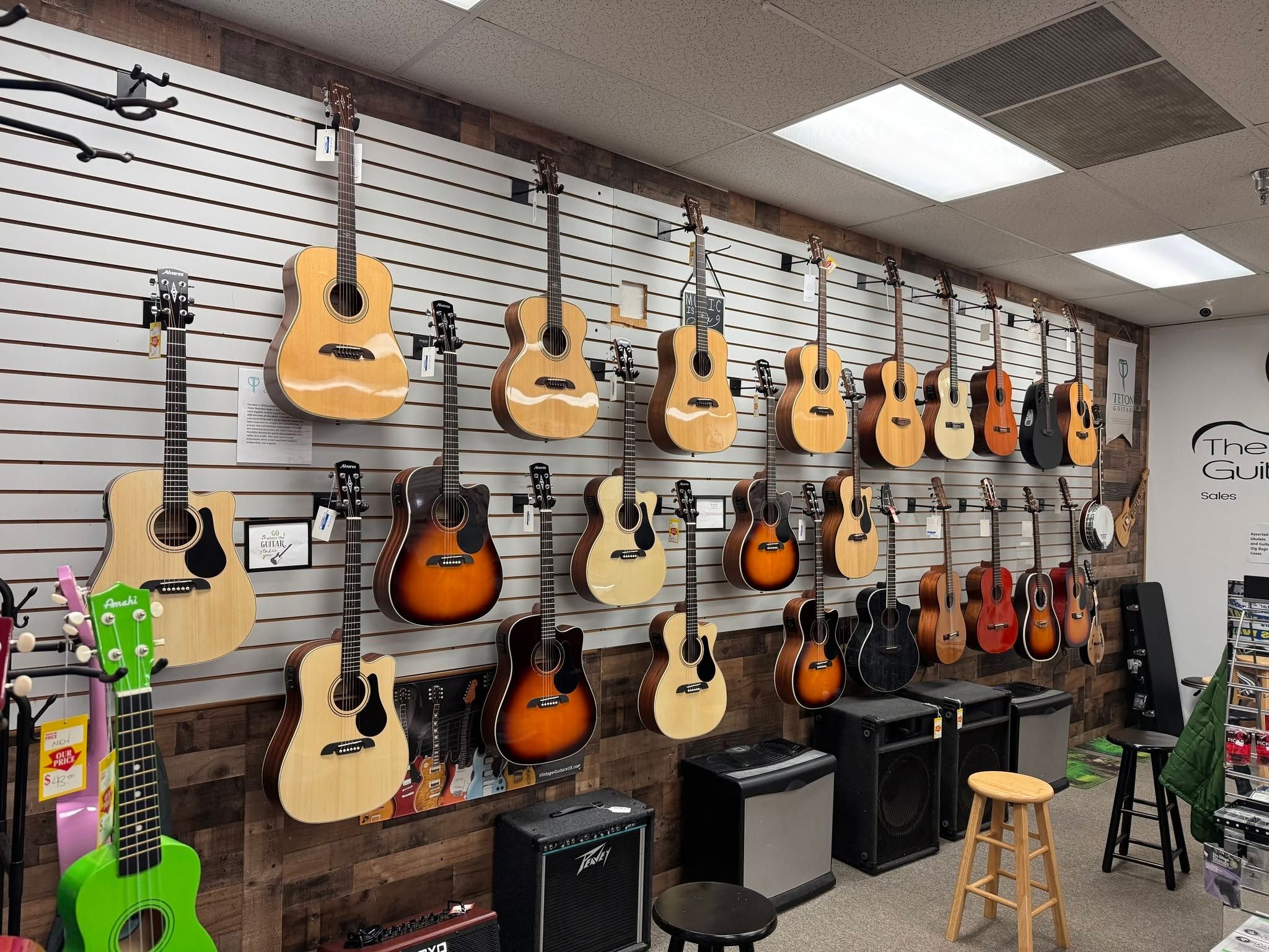 Rows of acoustic guitars in natural, sunburst, and mahogany finishes on the wall