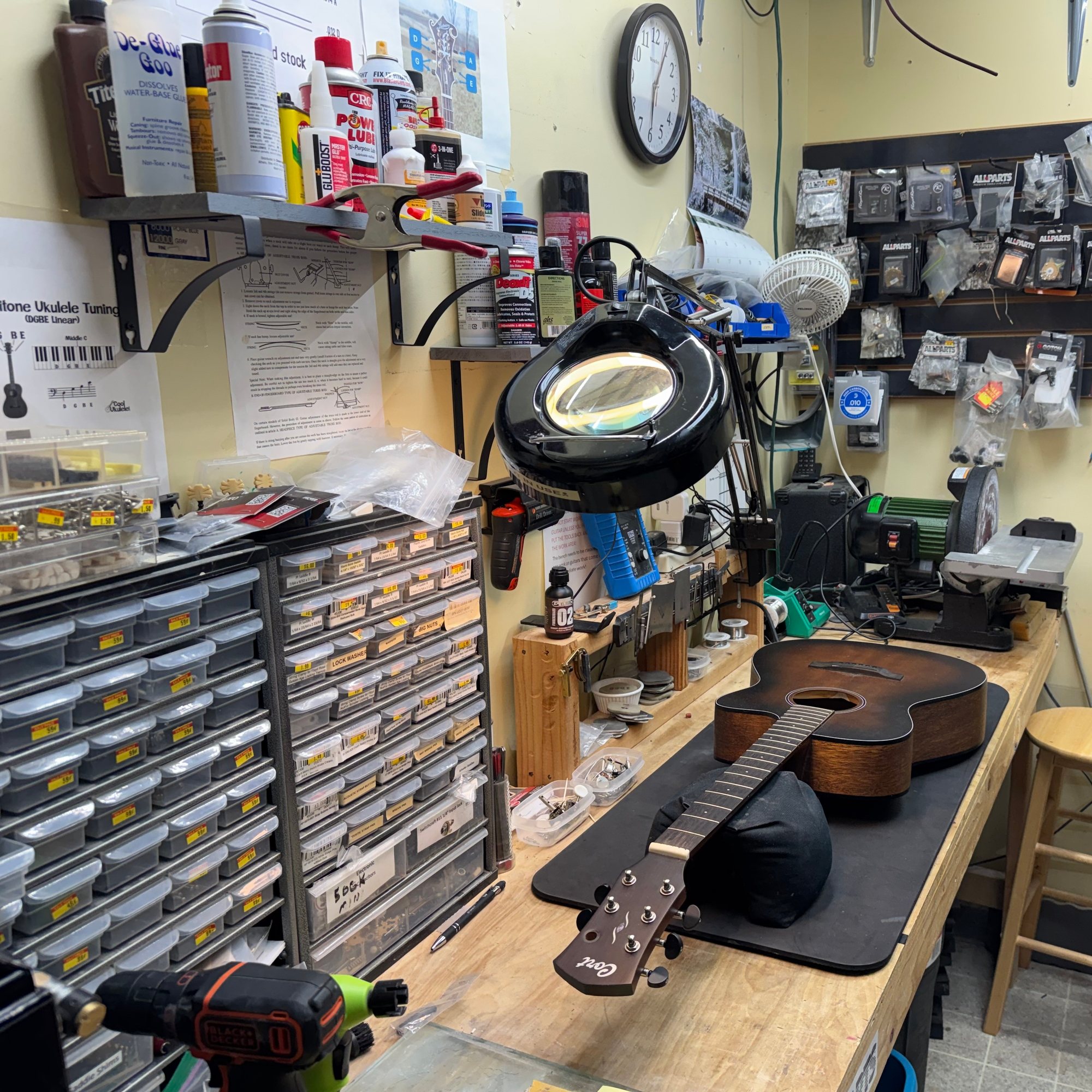 Acoustic guitar body and neck laid out on the repair bench beside a magnifier lamp