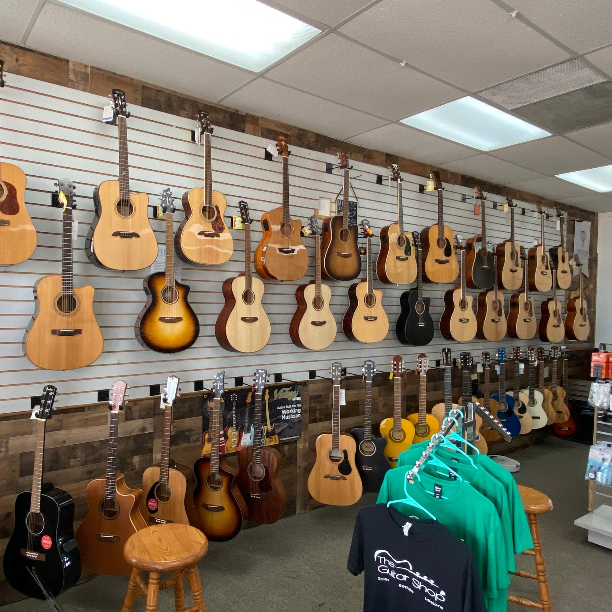Two rows of acoustic guitars hanging on the slatwall above reclaimed wood panelling