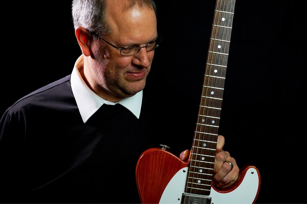 Mike Graebner looking down at the neck of an orange Telecaster style guitar