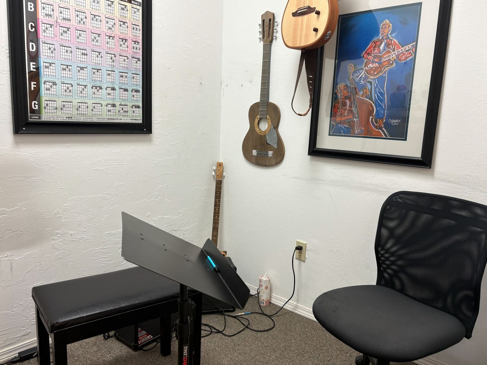 Lesson room corner with a wall-hung ukulele, bench and framed guitar painting