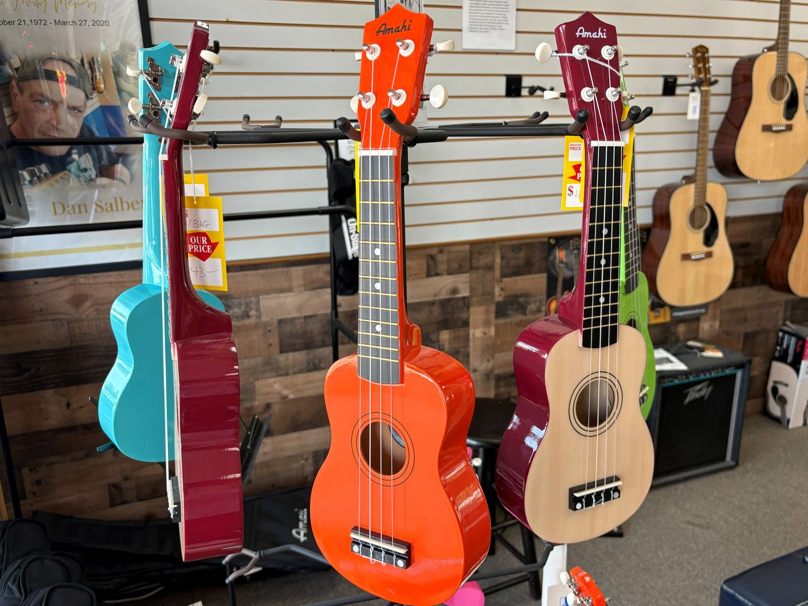 Brightly coloured soprano ukuleles in teal, red and orange hanging on a display rack