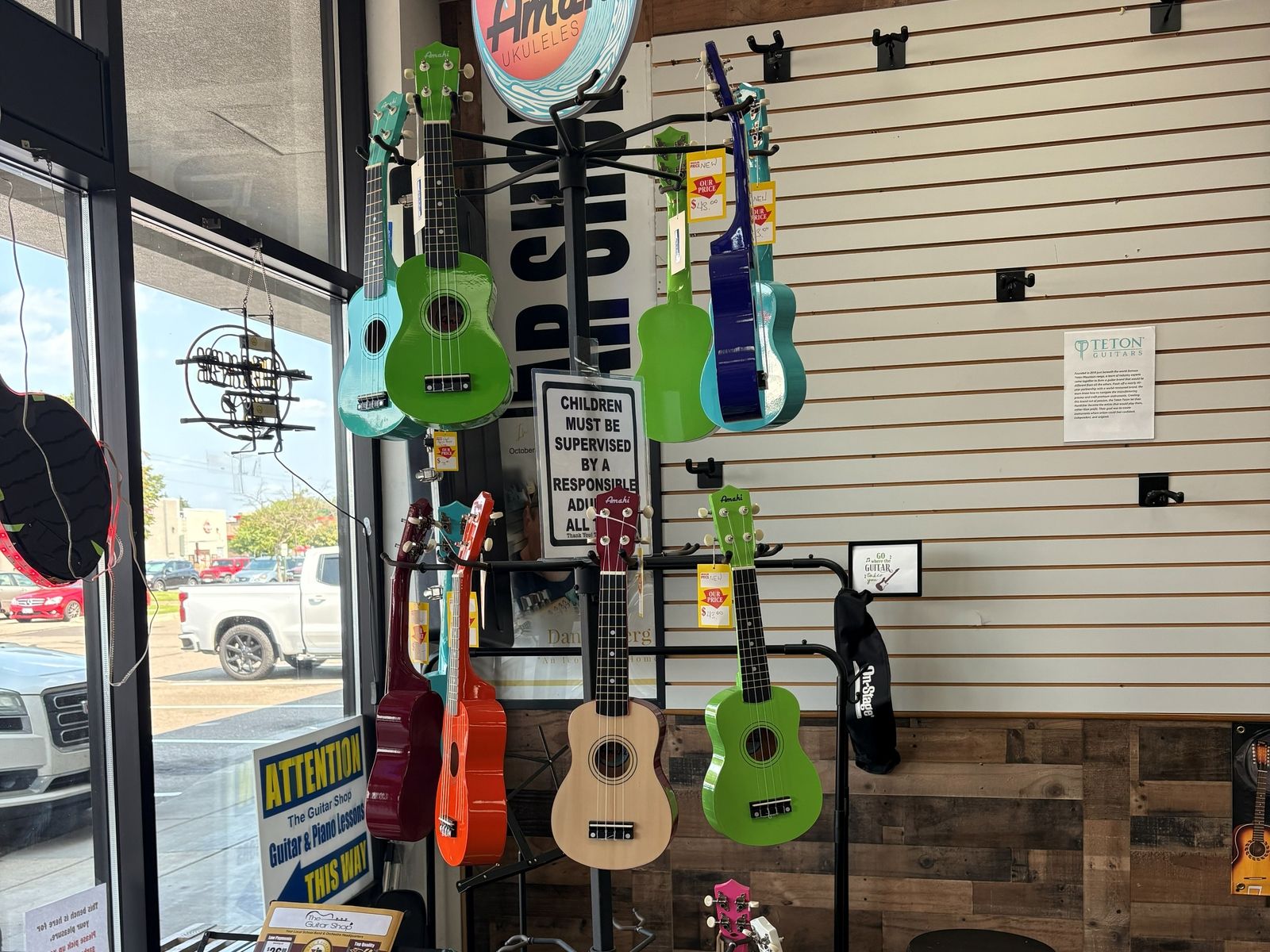 Ukuleles on stands in the front window under the Amahi sign, daylight behind them